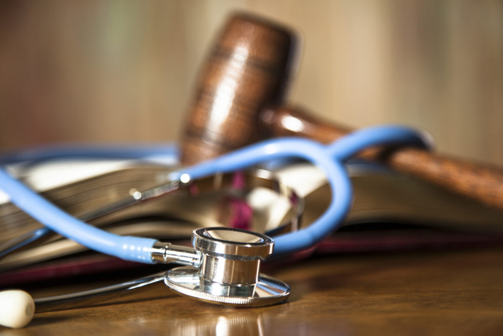 Wooden Judge's gavel and stethoscope with book lying on courtroom table.  Legal system, lawsuit, healthcare legislation, and medical concept.  No people.